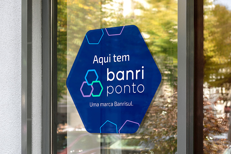 A imagem mostra um adesivo em uma porta de vidro, com os dizeres: Aqui tem Banriponto. Uma marca Banrisul